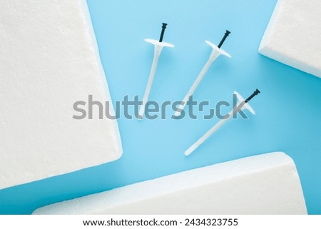New white plastic insulation anchor dowels and styrofoam panels on blue table background. Pastel color. Closeup. Material for house thermal protection. Home facade repair work preparation. Top view.