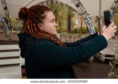 unusual mid adult woman with dreadlocks and freckles taking self portrait using phone outdoors in fall