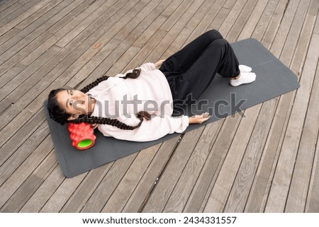 Serene image capturing young indian woman giving invigorating massage of her neck with massage roller on sunlit terrace, promoting wellness, relaxation, and self-care practices.