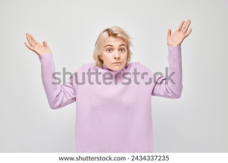 Confused young woman in a purple turtleneck shrugging with hands up, isolated on a white background