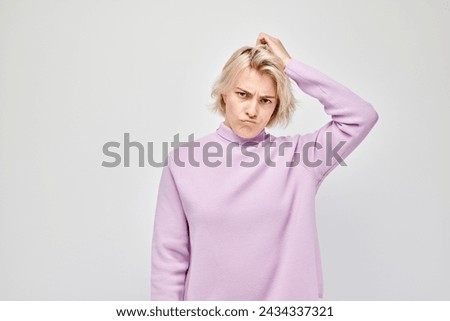 Confused young woman scratching her head, wearing a purple turtleneck on a white background.