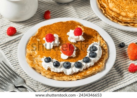 Sweet American Smiley Face Breakfast Pancakes with Whipped Cream and Berries Royalty-Free Stock Photo #2434346653