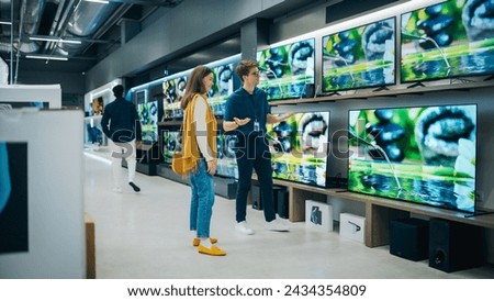 Beautiful Female Client Having a Conversation with Retail Home Electronics Shop Consultant. Young Woman is Shopping for a Modern TV Set. Customer Looking for a New Television in Department Store