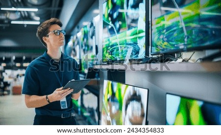 Young Sales Manager in Home Electronics Store Expertly Manages Operations Using Tablet Computer. Professional Oversees TV Sets Inventory and Product Updates with Technological Efficiency