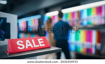 Close Up of a Red Sale Sign in a Home Electronics Department Store with a Range of Modern Smart TV Sets. Shoppers Explore Discounted Home Appliances in a Busy Retail Storefront Showroom