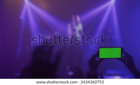 Silhouette of hands raised up with smartphone green screen at concert with bright stage lights