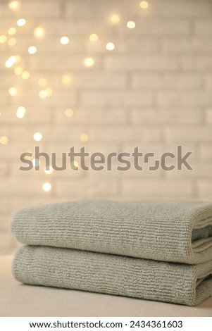 Stacked soft towels on white table near brick wall indoors, closeup. Space for text