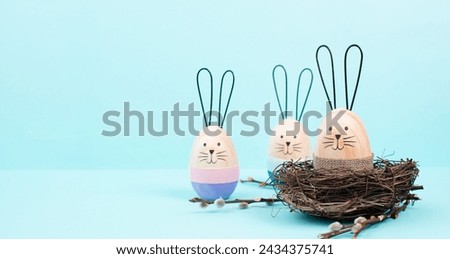 Easter bunny or rabbit sitting in a bird nest, willow branches, wooden egg, spring holiday, blue color 