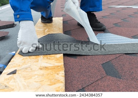 Against the background of a soft roof roof, a worker removes a protective film, for a tile sheet sticker