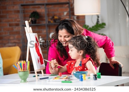 Indian mother and little daughter painting on easel together at home