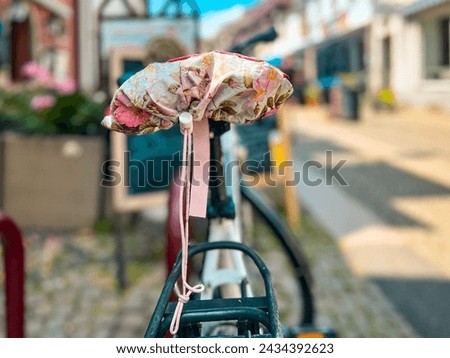Bicycle parked on a cobblestone city street. The bicycle seat is covered with a beautiful floral-patterned seat cover. Located in Breisach, Germany. Royalty-Free Stock Photo #2434392623