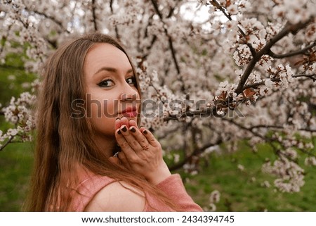 beautiful blond natural hair woman portrait in pink outfit is posing in botanical garden park near white blooming tree with flowers. Spring and purity, natural beauty. 