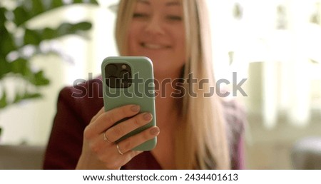 Woman looking at phone screen and laughing. Reading something amusing or receiving funny messages from friends. Viewing humorous or comedic photos, videos, or memes on social media or messaging apps. Royalty-Free Stock Photo #2434401613