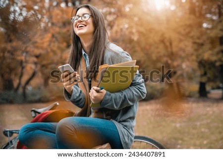 Young female college student sitting alone outdoors and laughing after reading very funny text message on her mobile phone.