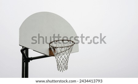 A single basketball hoop stands tall with its white backboard and orange rim, poised against a clear, pale sky, awaiting players to commence a game. Royalty-Free Stock Photo #2434413793