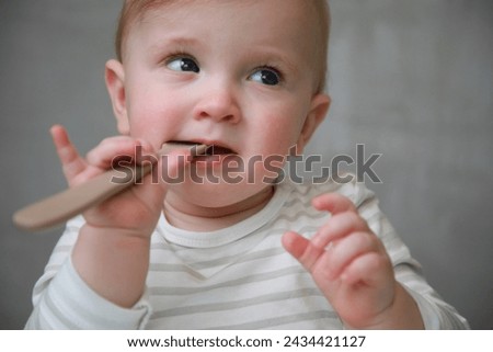 Portrait of a beautiful 10 months baby girl eating on grey background with natural light and complementary colors: Concept of health, childhood, eating, growth