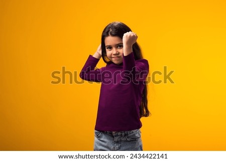 Portrait of enraged Child girl showing fist at camera on yellow background. Negative emotions concept Royalty-Free Stock Photo #2434422141