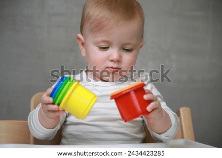 10 months baby girl playing with colorful plastic toy elements on a neutral grey background: Concept of development, play, growth, attention Royalty-Free Stock Photo #2434423285