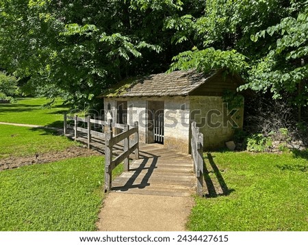 Historic Spring House exterior in the recreated and restored 1800 Pioneer Village at Spring Mill State Park, near Mitchell, Indiana with beautiful blue sky and vivid green trees and grass copy space. Royalty-Free Stock Photo #2434427615
