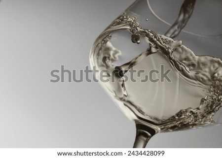 Pouring tasty aromatic wine in glass on gray background, closeup. Space for text