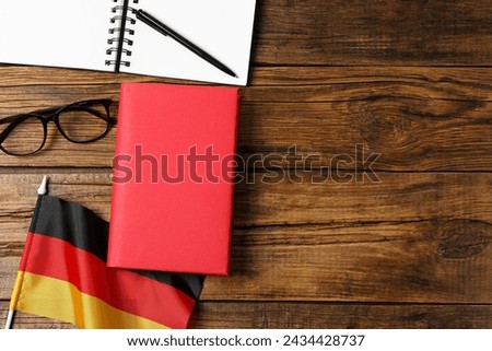 Learning foreign language. Flag of Germany, book, glasses and stationery on wooden table, flat lay with space for text