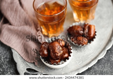 Dates or dried dates and hot tea on silver tray.  Royalty-Free Stock Photo #2434474381