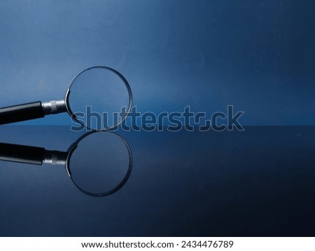 Reflection magnifying glass on a black acrylic board with blue background and copy space.