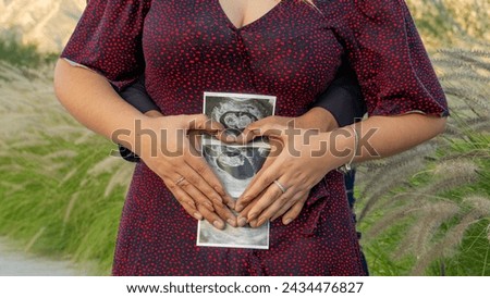 Young Hispanic couple embracing, showing a printed ultrasound surrounded by their hands forming a heart, general shot, mexico, no faces