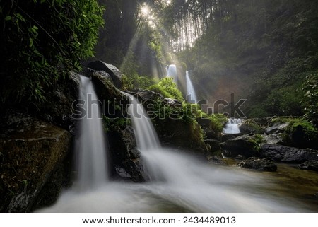 The atmosphere of a waterfall in the morning flowing in the middle of the forest between rocks