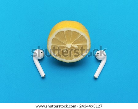 Half a lemon with wireless headphones on a blue background. The concept of listening to music tracks. Royalty-Free Stock Photo #2434493127