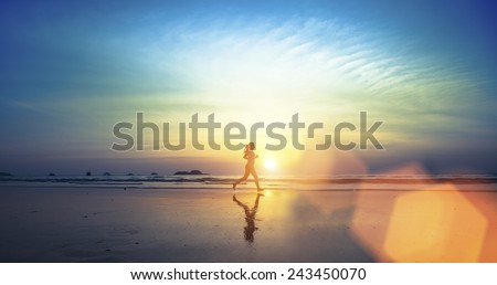  Silhouette of a young girl running along the beach of the sea during an amazing sunset. Royalty-Free Stock Photo #243450070