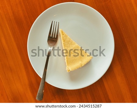 Cheesecake slice, New York style classical cheese cake on wooden background. Slice of tasty cake on white plate served with dessert fork. Top view