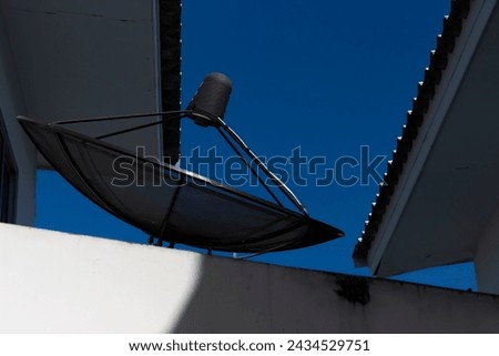 Picture of a television transmitting dish behind a house. Bright blue sky background.