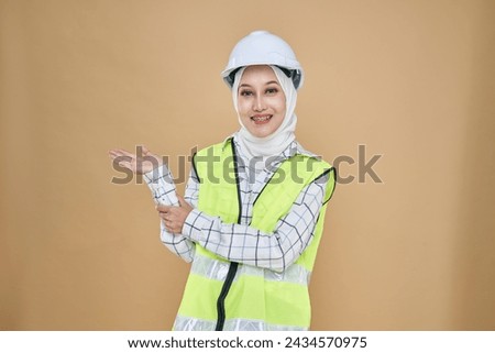 Asian hijab girl engineer in yellow  vest and wearing a safety helmet, give a right direction hand gesture isolated on background in studio.