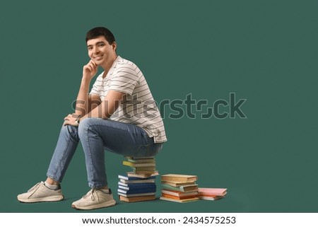 Thoughtful young man sitting on books against green background