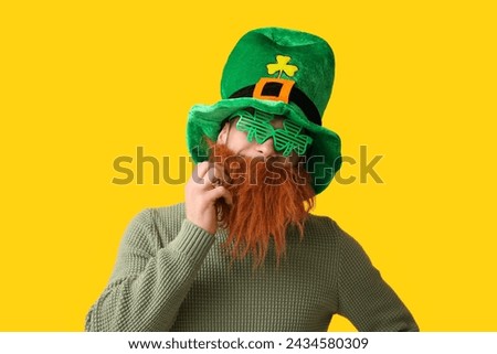 Funny bearded man in leprechaun hat and decorative glasses in shape of clover on yellow background. St. Patrick's Day celebration