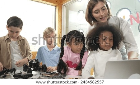 Caucasian teacher praise student while looking at learner work or presentation. Group of diverse student looking at presentation and fixing motherboard at table with chips and wires placed. Erudition. Royalty-Free Stock Photo #2434582557