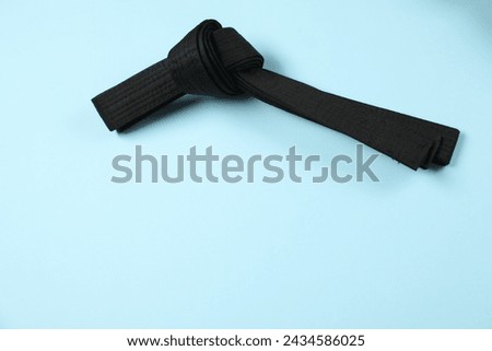 Black karate belt on light blue background, top view. Space for text Royalty-Free Stock Photo #2434586025