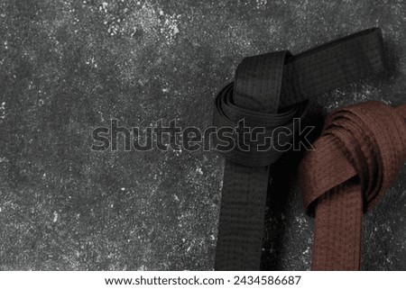 Black and brown karate belts on gray textured background, flat lay. Space for text Royalty-Free Stock Photo #2434586687