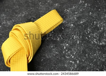 Yellow karate belt on gray textured background, space for text Royalty-Free Stock Photo #2434586689