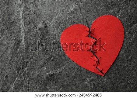 Broken heart. Torn red paper heart sewed with thread on dark grey table, top view. Space for text Royalty-Free Stock Photo #2434592483
