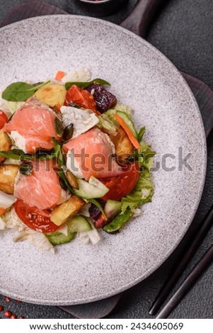 Delicious juicy salad with salmon, tomatoes, cucumber, herbs, pumpkin seeds, salt and spices in a ceramic plate on a dark concrete background