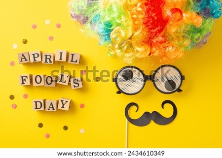 Snapshot of wooden letters spelling "April Fool's Day," confetti with party accessories like clown's wig, eyeglasses, and mustache, creating a humorous face on a bright yellow surface Royalty-Free Stock Photo #2434610349