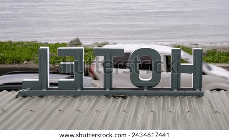 Large retro hotel sign on tinned roof with passing traffic overlooking ocean on tropical island destination in Southeast Asia