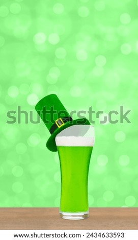 Glass of green beer with leprechauns green top hat on green blurred background. Saint Patrick's Day Concept. Empty space for text