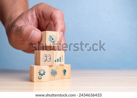 Hand placing the final wooden block with a target icon on a stack symbolizing business growth and goals.
