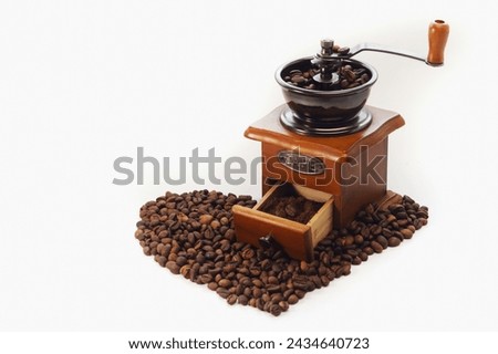 Manual coffee grinder on a white isolated background. Copy space. Coffee beans laid out on the surface in the shape of a heart.