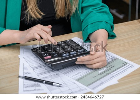 A woman working in an accounting office counts on a calculator and fills out tax returns, translation: official government income declaration form Royalty-Free Stock Photo #2434646727