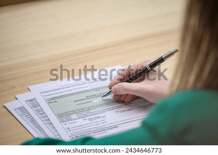 A woman fills out the Polish PIT tax declaration form, translation: official government income declaration form Royalty-Free Stock Photo #2434646773