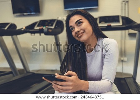 Young woman, gym and smile with phone, social media or chatting on web, app or internet on break from workout. Woman, smartphone and fitness with comic meme, funny video or social network at training.